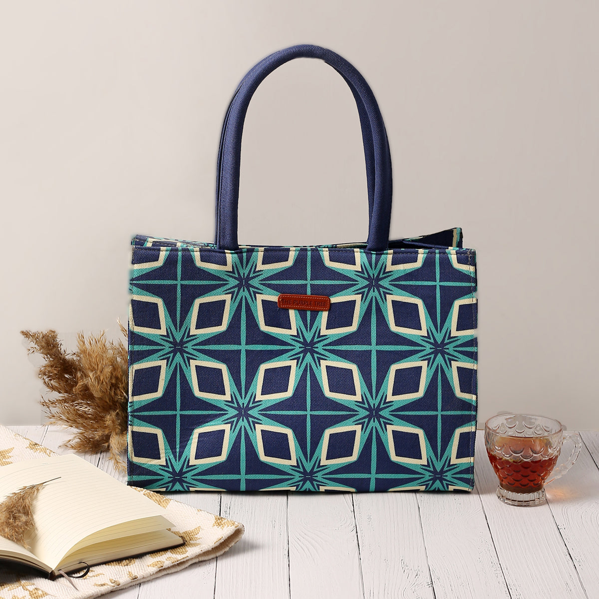 Blue and green patterned tote bag with book and sunglasses.