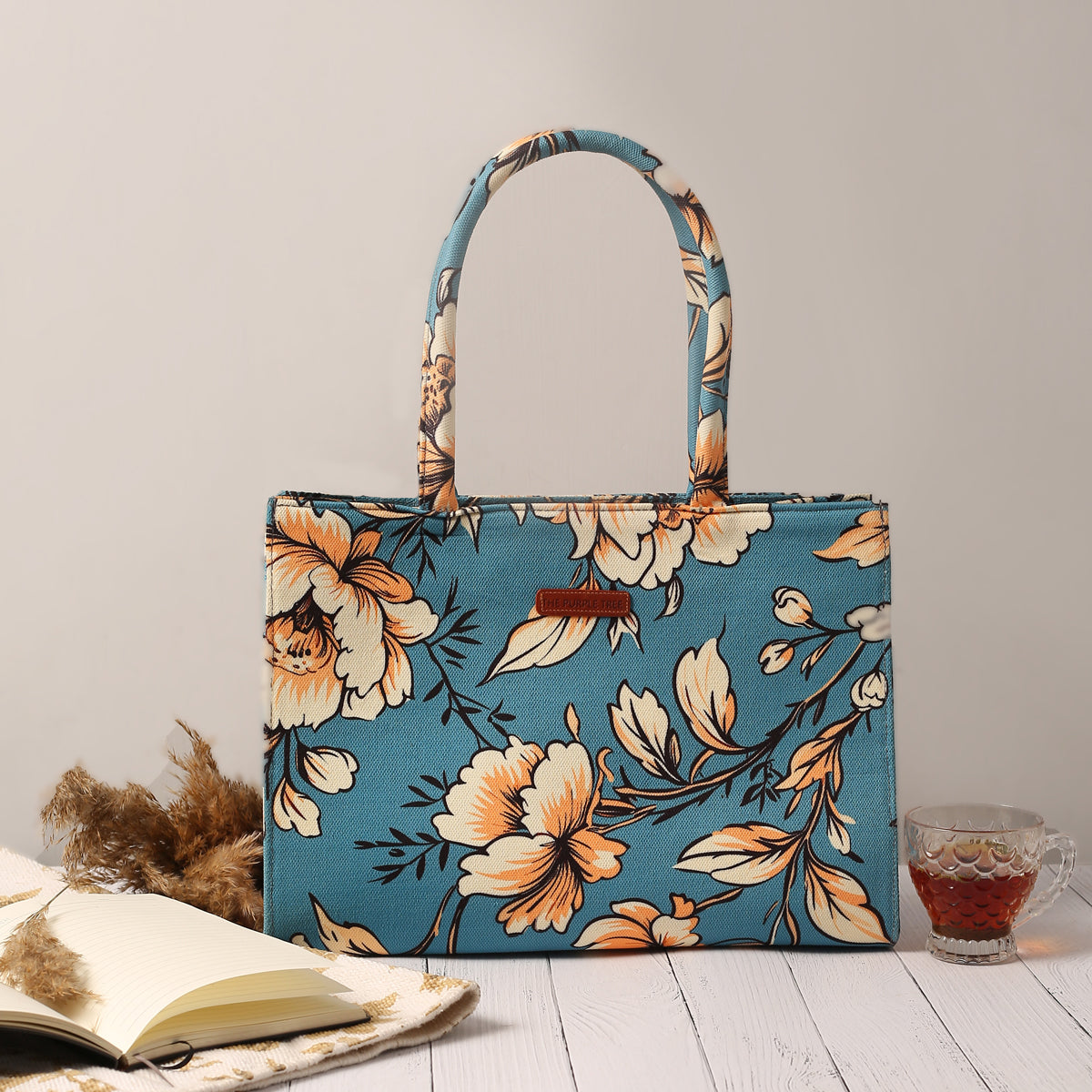 Floral print tote bag with book and notebook on wooden table.