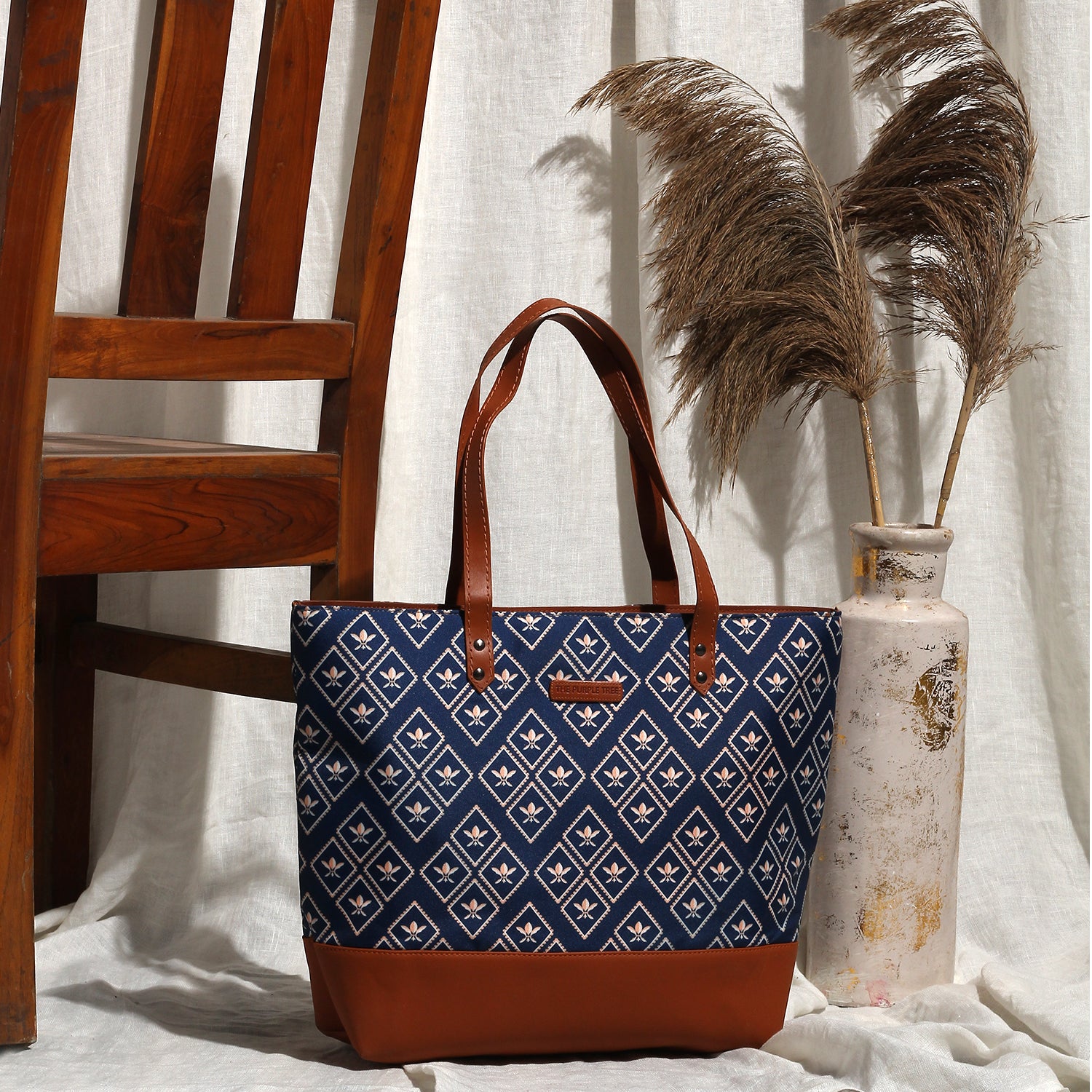 A stylish tote bag in blue and brown, placed next to a wooden chair. Perfect for carrying your essentials in style.