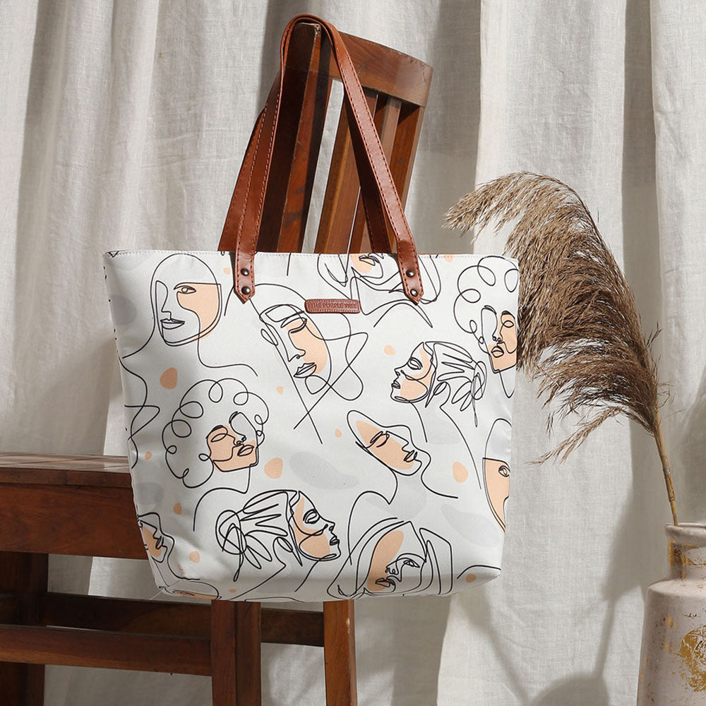  White tote bag with women's faces pattern, stylish accessory for any outfit.