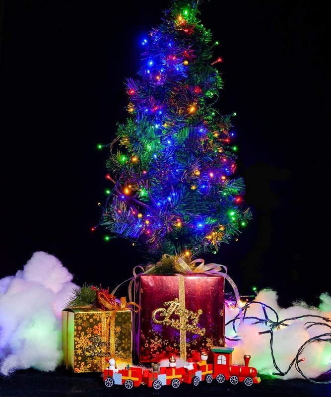  Christmas tree illuminated with lights and surrounded by gifts on black.