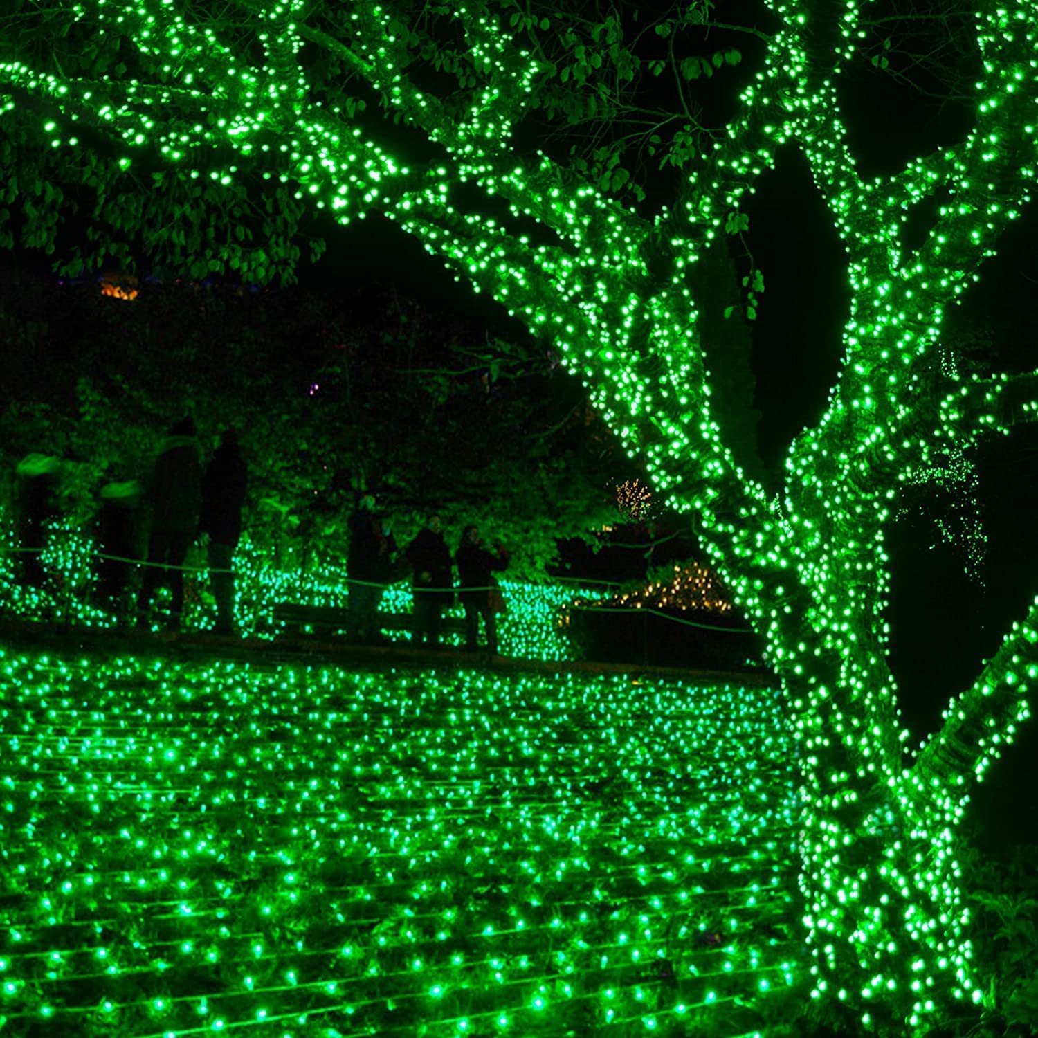 A festive green tree adorned with twinkling lights stands in the center of a park.