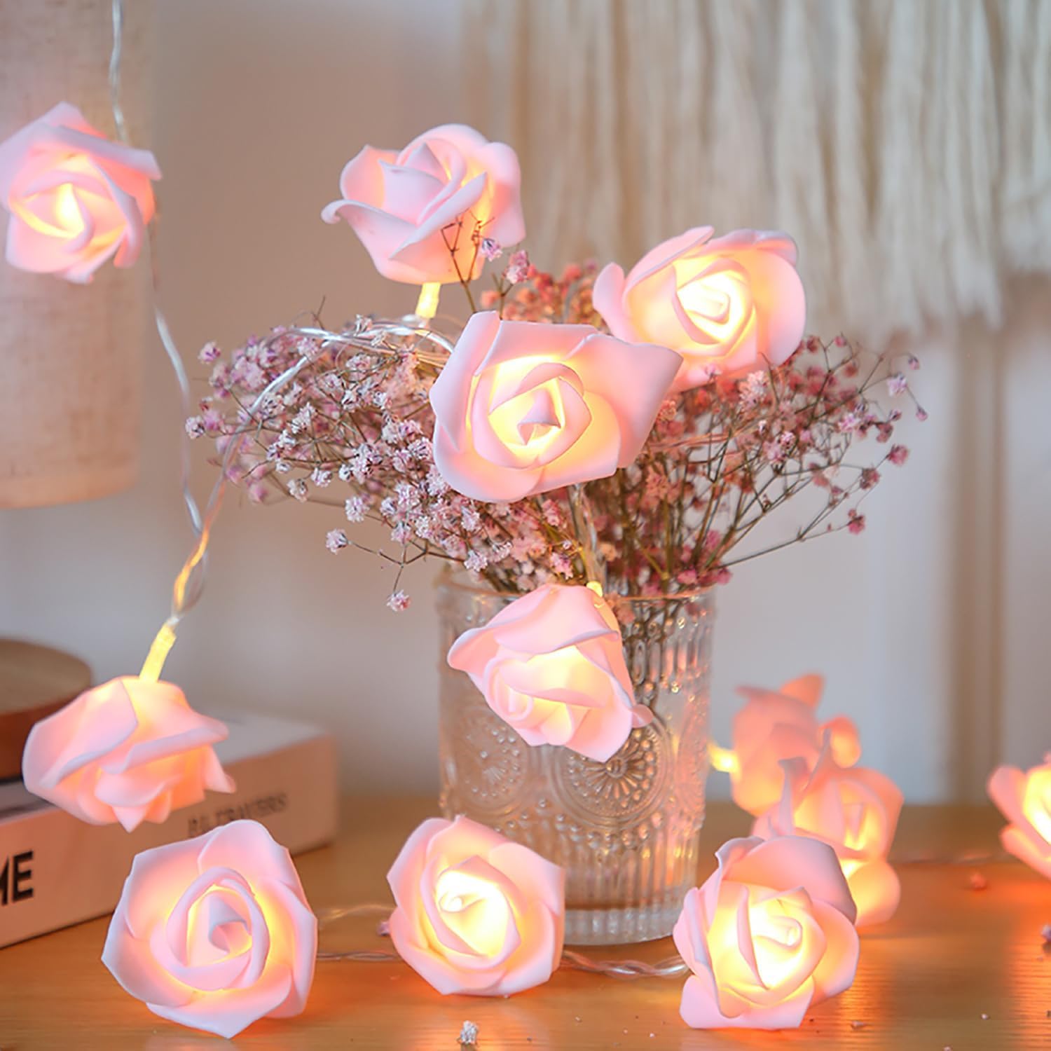 A vase of pink roses next to a book on a table.