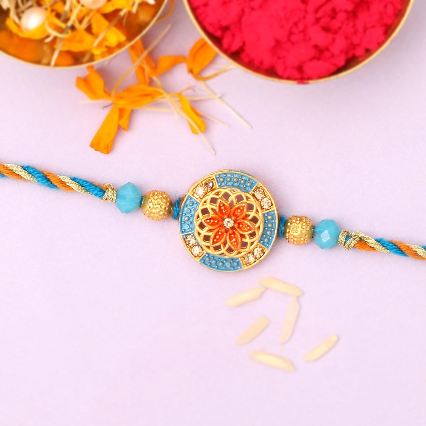 A gold and blue rakhi with a flower design on a white background.