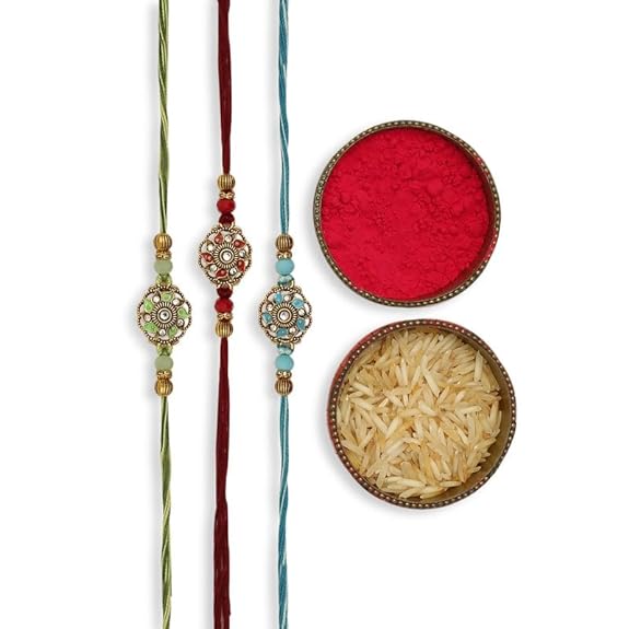 Three rakhi's in different colors with gold and green beads, accompanied by vermilion and a bowl of rice.