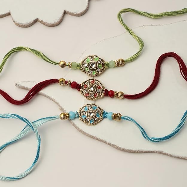 Three rakhi's with gold and green beads: one red, one blue, and one yellow.