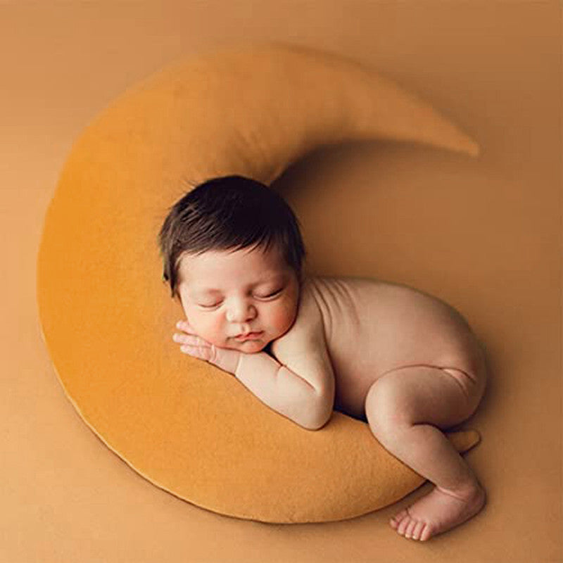 1. A newborn peacefully sleeping on a crescent moon-shaped pillow.