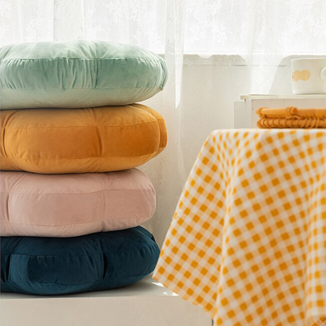 Pillows in stack on table next to yellow and blue checkered tablecloth.