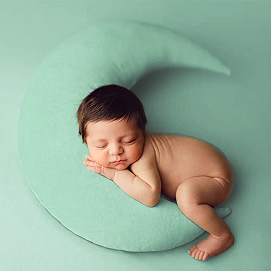 A peaceful baby girl sleeping on a green crescent pillow, dreaming sweet dreams.