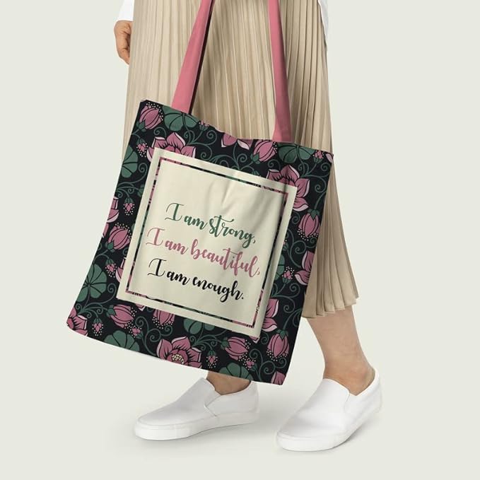 Women carrying a Black tote bag with a quote: ""I am strong, I am beautiful, I am strong"" surrounded by green and pick florals with pink color matching handle