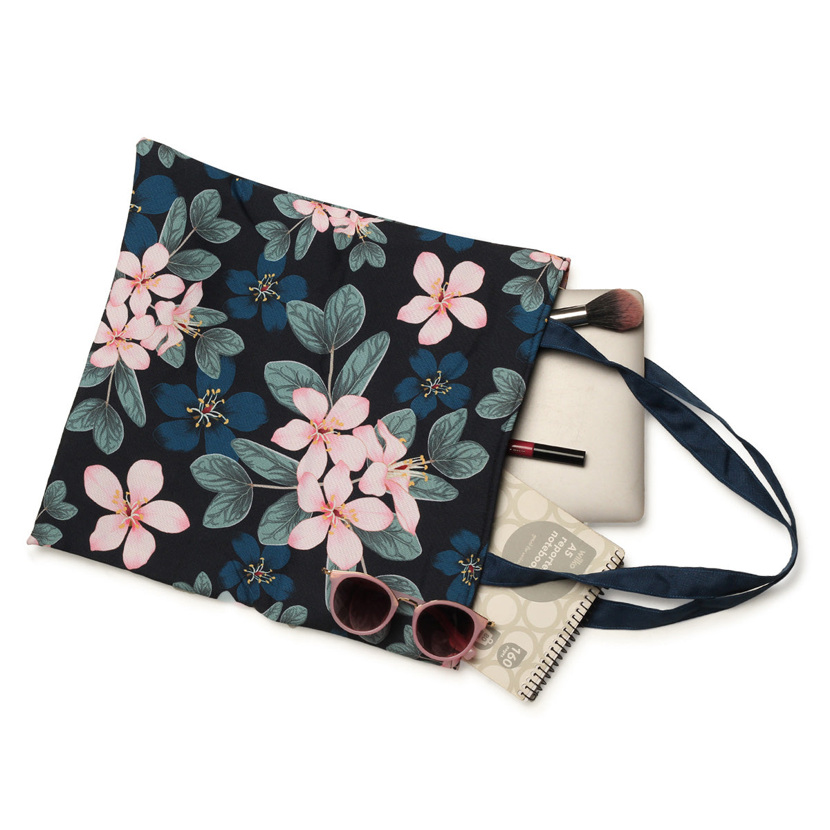 A navy blue tote bag with pink floral print, sunglasses, a notebook, and makeup brush.