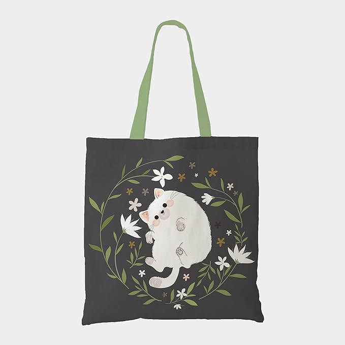 A stylish tote bag adorned with a white cat nestled among a variety of blooming flowers, showcasing a playful aesthetic.
