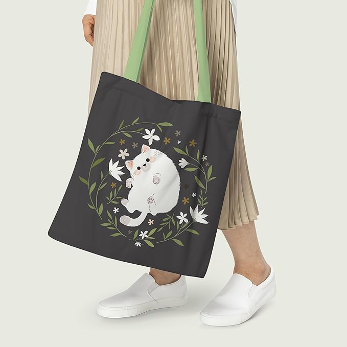 A tote bag displaying a white cat at the center of a floral arrangement, blending nature and charm in its design.