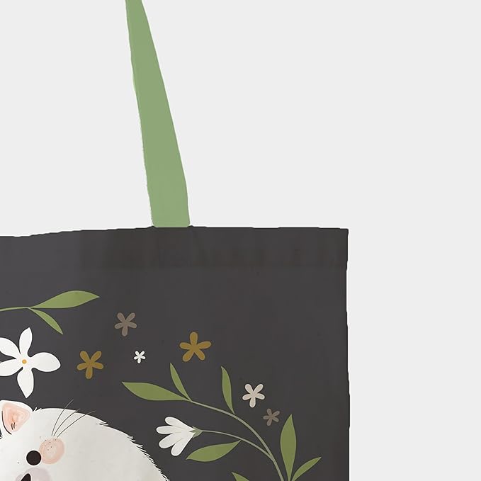 A tote bag illustrated with a white cat surrounded by an array of flowers, offering a delightful and whimsical appearance.
