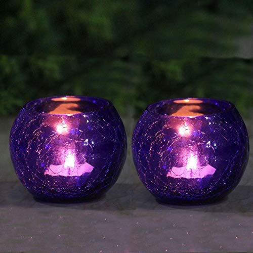 Two purple glass tealights with flickering candles, casting a warm and cozy glow in a dimly lit room.