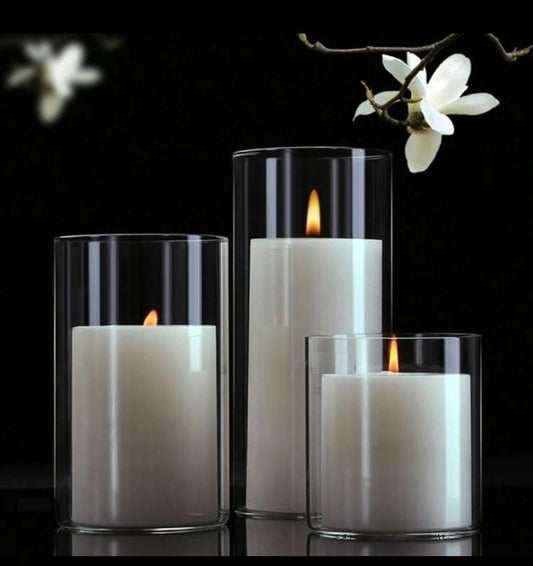 Three glass candles with white flowers in the background, creating a serene and elegant ambiance.