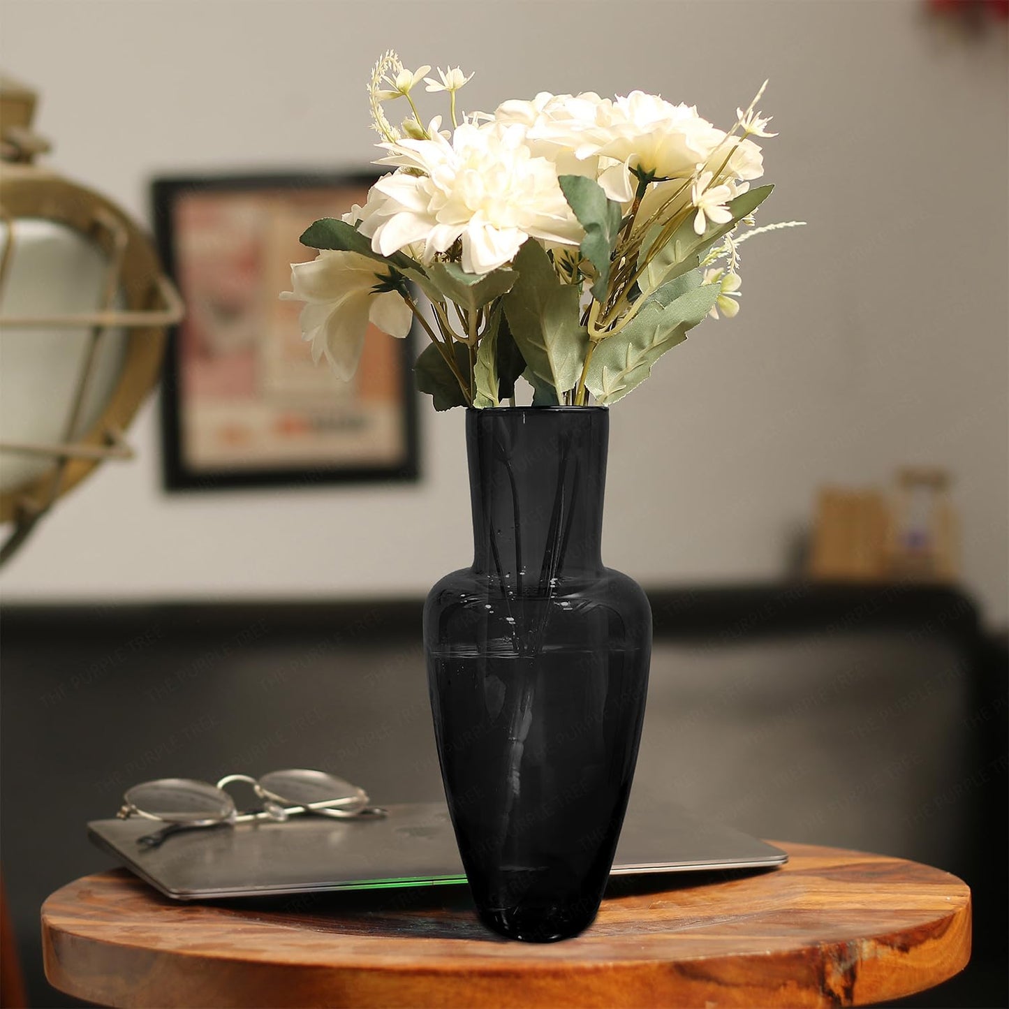 A black vase filled with white flowers elegantly placed on a wooden table.
